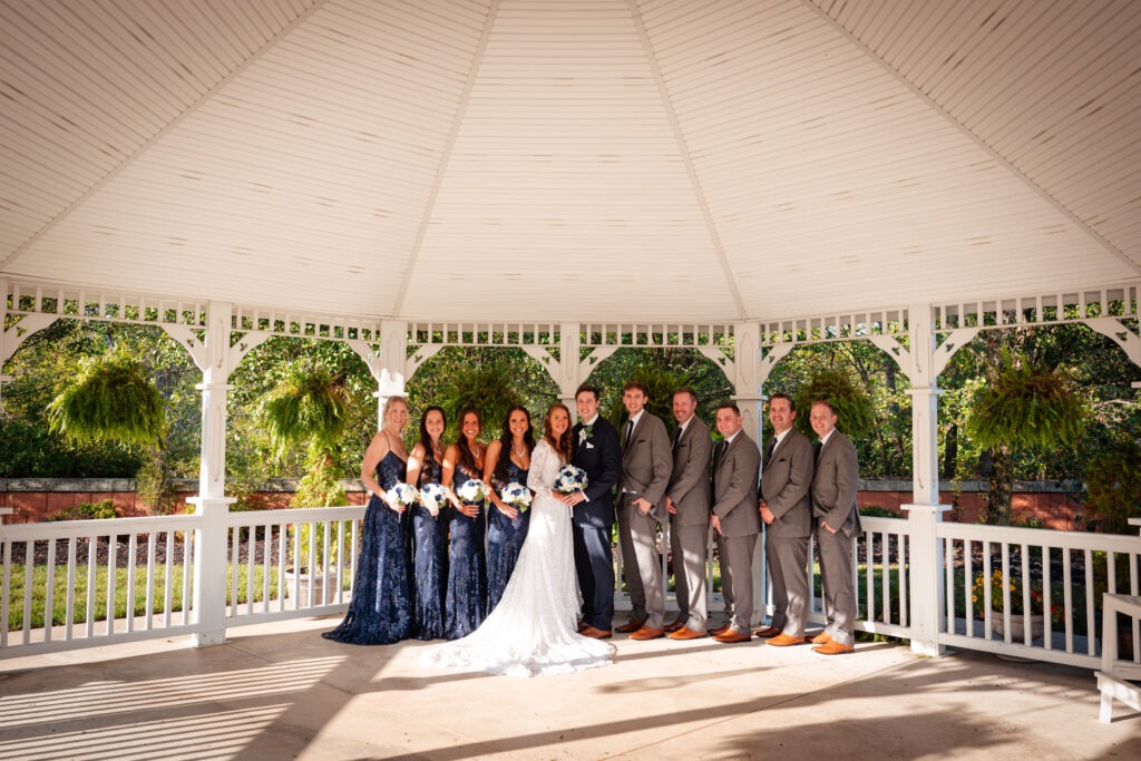 Bridal party posed in a gazebo, featuring the bride in a white gown and bridesmaids in navy dresses