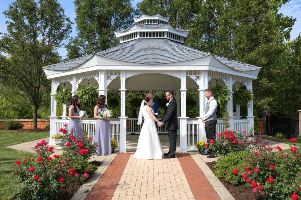 A wedding ceremony in a gazebo, featuring a bride and groom exchanging vows