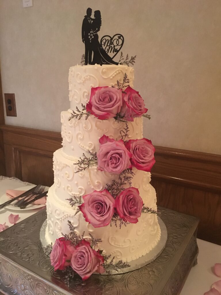 A four-layer white cake with pink roses on each layer, displayed at the event center.